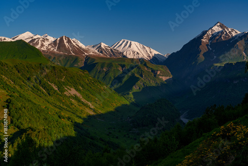 Fotografia Snowy Caucasus peaks above deep green valley in clear morning light