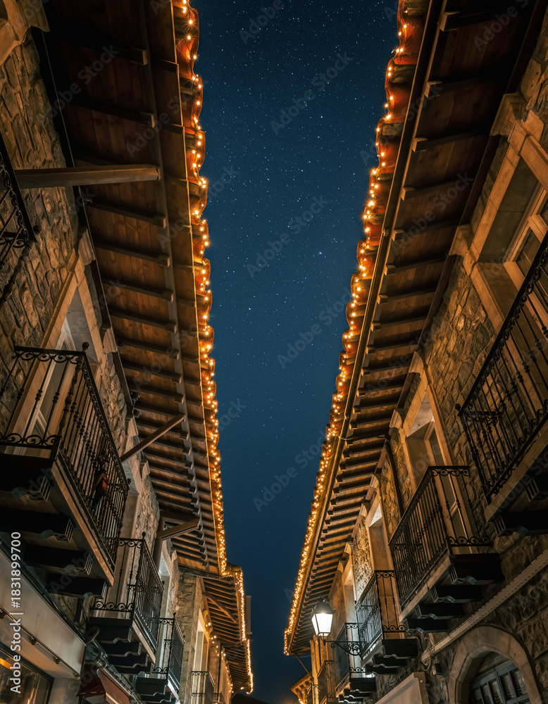 Obraz premium calle estrecha de un casco antiguo, iluminada con luces navideñas cálidas que bordean los tejados y balcones de edificios de piedra y madera, creando un ambiente festivo y acogedor durante la noche.