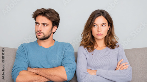 Unhappy young caucasian couple sitting back to back on sofa with arms crossed after argument