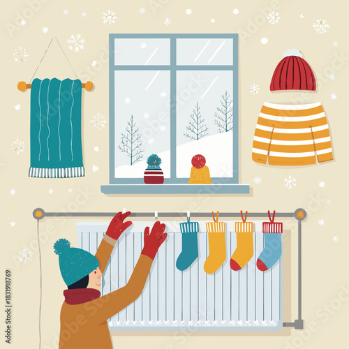 Una persona cuelga calcetines y ropa de invierno sobre un radiador, mientras afuera la nieve cubre el paisaje visto por la ventana.
