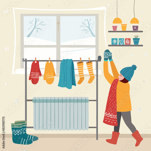 Una niña seca su ropa de invierno en un soporte junto al radiador, en una habitación cálida con vista a un paisaje nevado a través de la ventana.