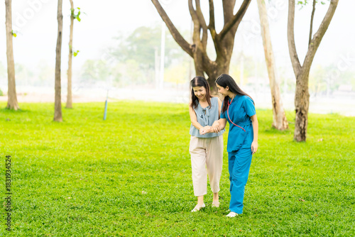 Asian nurse and elderly female patient standing in park and holding hands. Concept of care for elderly in retirement. Health service center.