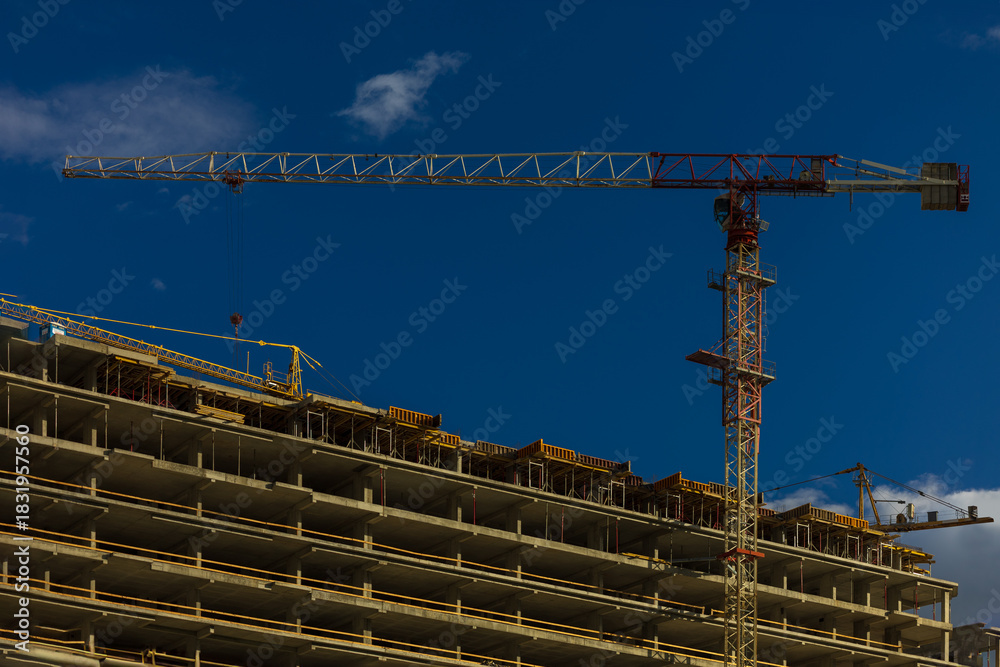 Naklejka premium Construction cranes and new buildings, construction work of modern skyscrapers on a sunny day.