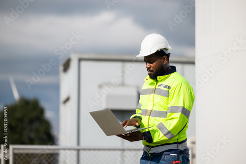 African Engineer man working on tablet computer in field with wind turbines background, Windmill. environmental renewable clean energy. Wind power generation. Windmill engineer inspection progress