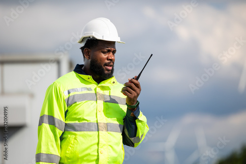 African Engineer man working on tablet computer in field with wind turbines background, Windmill. environmental renewable clean energy. Wind power generation. Windmill engineer inspection progress