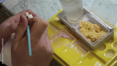 Dental technician applying primer on dental mold model using brush for prosthetics, laboratory tools, dentistry education, prosthodontics, oral restoration.