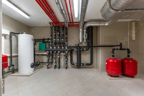 Bright and clean utility room showcasing a modern plumbing and heating system. Red pipes, tanks, and valves are arranged neatly on the walls for easy access and maintenance.