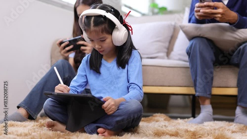 Asian family spending time together in the living room, each absorbed in their own digital device, technology addiction and lack of communication in a home environment.