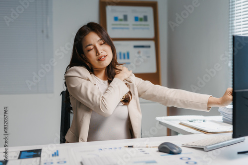 Asian businesswoman experiencing neck and shoulder pain, stretching during long hours working on computer at office