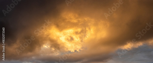 Epic panoramic view golden rain clouds during sunset or sunrise breaking through dark storm clouds creating powerful heavenly background with bright light