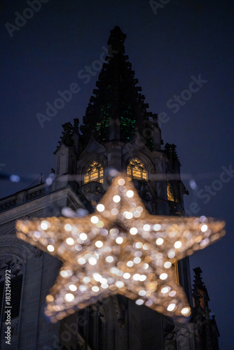 During the Christmas season, illuminated stars hang in front of the Münster unserer lieben Frau's illuminated tower walls, which shine at night. Constance, Baden-Württemberg, Germany.