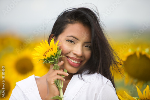 Fotografie A beautiful mulatto Latin woman with a white shirt brings it close to her face and flirts with a sunflower