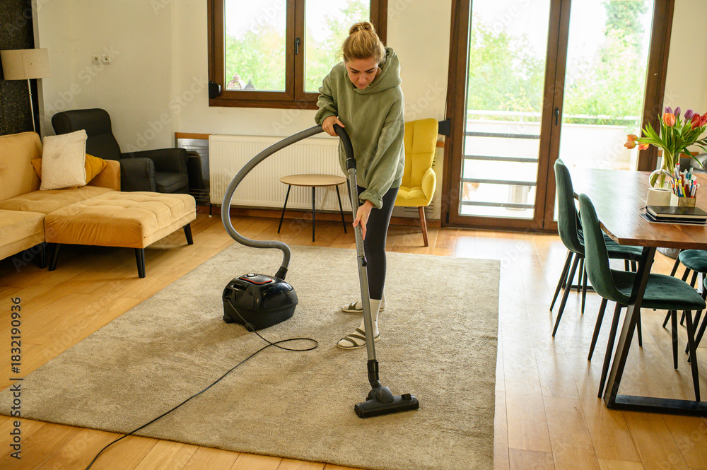 Fototapeta premium Young woman cleaning her home, making the bed, wiping glass surfaces, vacuuming and dusting. Housekeeping routine, cleanliness, home care, everyday domestic lifestyle