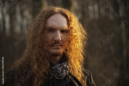 Portrait of a man with long curly hair in a forest during golden hour