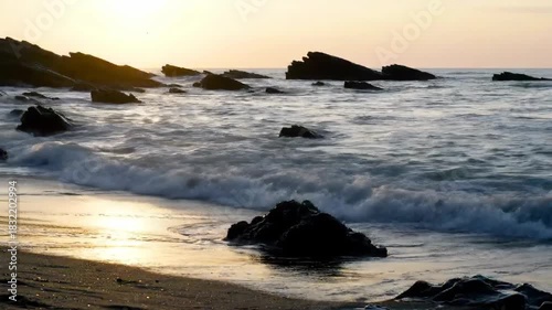 Ocean waves crash on rocky shore at sunset with soft light