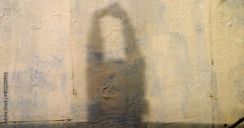 Shadow of a man projected onto the wall of a building. He is stretching his arms, under the warm orange light of dawn in the city. Medium shot.