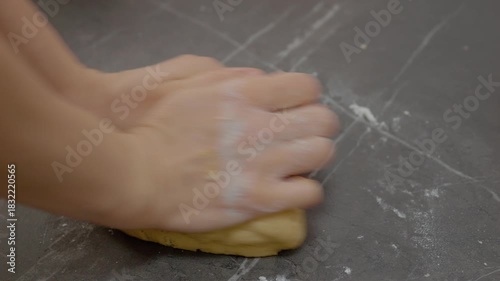 A woman's hands knead soft cookie dough on a smooth countertop, preparing for baking. Flour and dough create a fun, messy atmosphere in the kitchen.