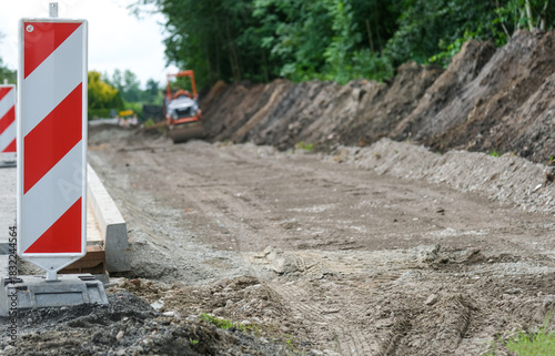 Detail Blick auf eine Straßenbaustelle mit laufenden Sanierungsarbeiten an aufgerissener Straße mit Copy Space im Vordergrund, Baumaterial, Absperrung, Maschinen und Erdarbeiten , selektiver Fokus