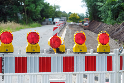 Detail Blick auf eine Absperrung einer Straßenbaustelle mit Sanierungsarbeiten an aufgerissener Straße, Baumaterial, Absperrung, Maschinen und Erdarbeiten, selektiver Fokus