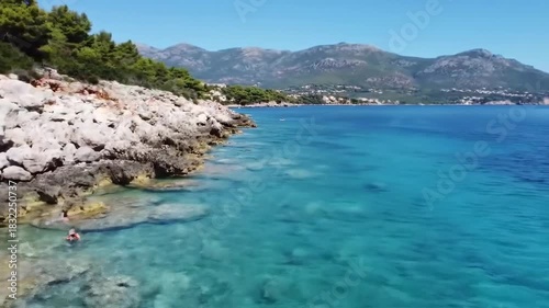 Vibrant blue ocean water meeting rocky coastline with distant mountain range under clear sky
