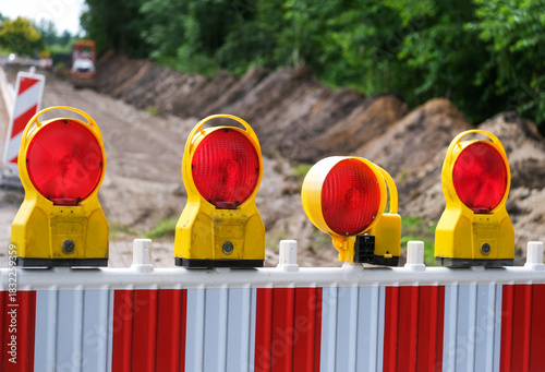Detail Blick auf eine Absperrung einer Straßenbaustelle mit Sanierungsarbeiten an aufgerissener Straße, Baumaterial, Absperrung, Maschinen und Erdarbeiten, selektiver Fokus