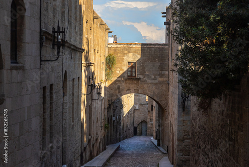Fototapeta Naklejka Na Ścianę i Meble -  Historic cobblestone Street of the Knights in the Medieval City of Rhodes, Greece, featuring stone architecture, soft afternoon light and a timeless medieval atmosphere
