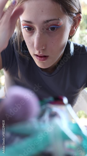 Caucasian girl brushing her eyebrows with a brush and painting her eyelids with orange eyeliner.