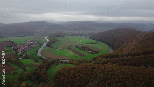 Aerial view of a picturesque, autumn landscape with a gloomy atmosphere and a small German village nestled on the banks of a river winding through the mountains. A gloomy autumn day in the Harz mounta