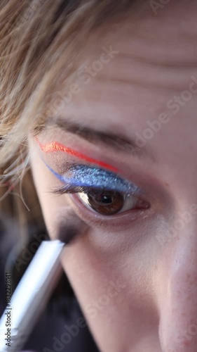 a Caucasian girl applying make-up to her lower eyelid with a brush