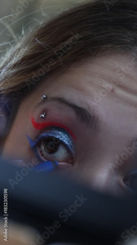 A Caucasian girl applying blue eyeliner to her lower eyelid, vertical shot in slow motion.