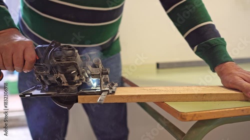 Side view of woodworker’s hands cutting a long wooden board with a power circular saw in a workshop