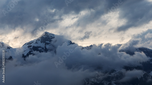 Der schneebeckte Gipfel des Großen Wiesbachhorns in Salzburg, Österreich in den Alpen (Glocknergruppe, Hohe Tauern),  eingehüllt in Wolken am Abend mit der Sonne hinter dem Berg.