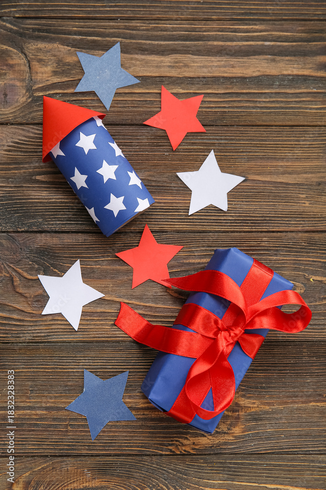 Fototapeta premium Firework rocket with gift box and stars on brown wooden background. American Independence Day