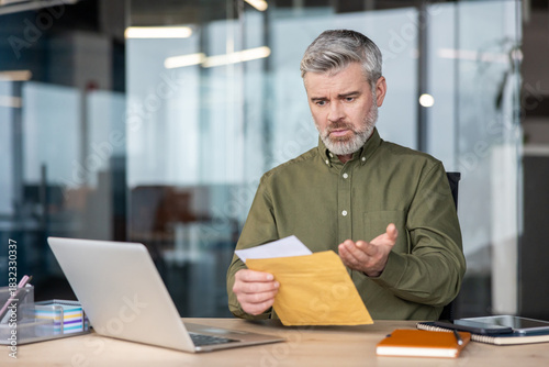 Cuadro en lienzo Mature businessman sitting at his desk, opening a document from an envelope and