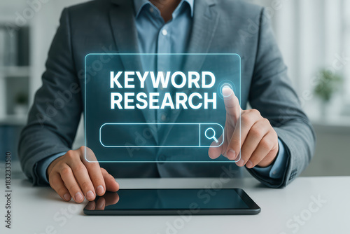 Keyword research concept with businessman in suit interacting with futuristic holographic interface and digital tablet on white desk in modern office