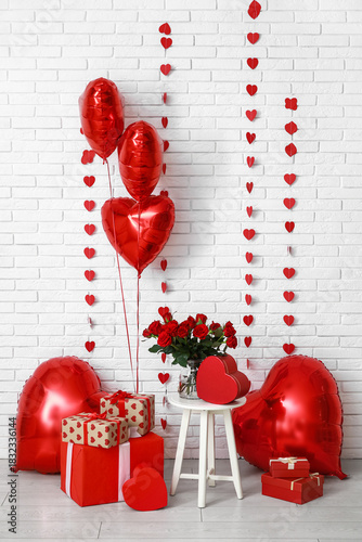 Heart shaped air balloons with gift boxes and bouquet of red roses near white brick wall. Valentine's day celebration