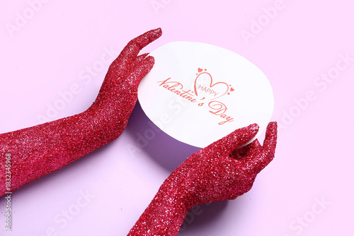 Female hands covered with glitter and greeting card for Valentine's Day on lilac background, closeup