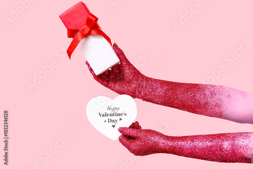 Painted female hands with greeting card and gift for Valentine's Day celebration on pink background, closeup