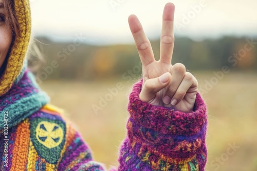 A person wears a colorful sweater and holds up two fingers in a peace sign.