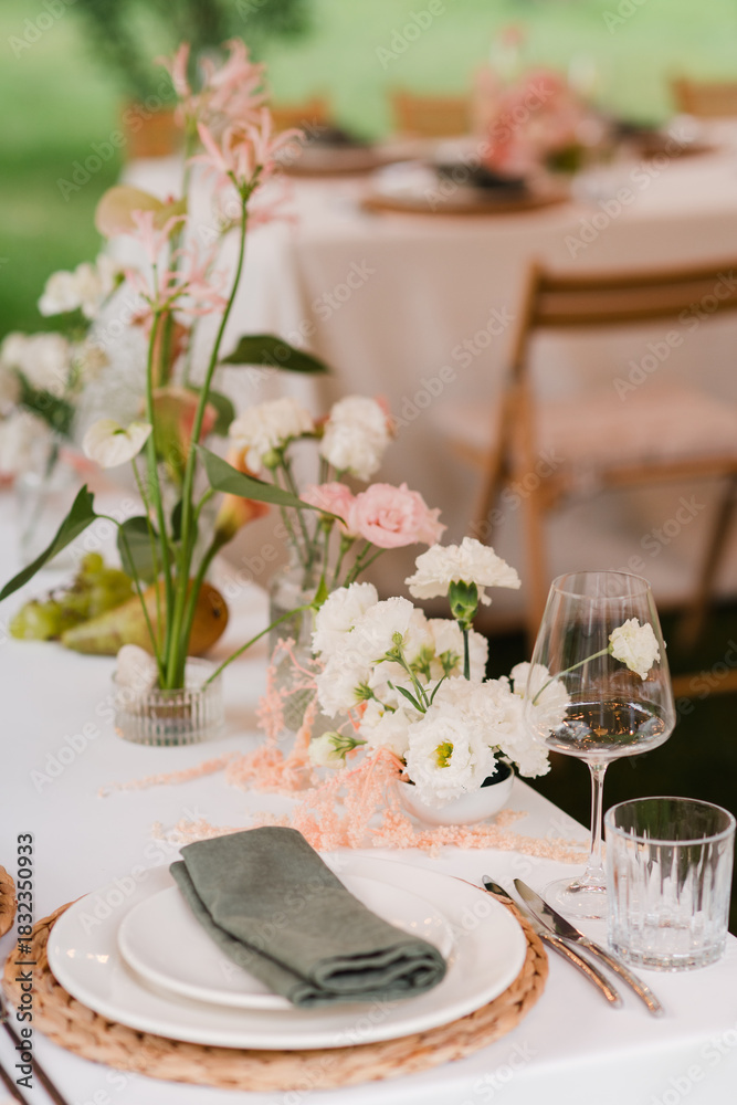 Fototapeta premium Coziness and style. Modern event design. Table setting at wedding reception. Floral compositions with beautiful flowers and greenery, candles, laying and plates on decorated table.