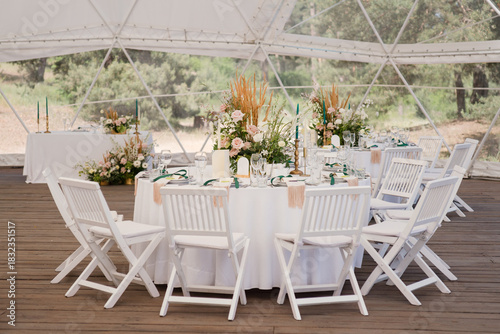 Coziness and style. Modern event design. Table setting at wedding reception. Floral compositions with beautiful flowers and greenery, candles, laying and plates on decorated table.