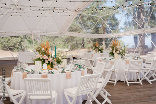 Coziness and style. Modern event design. Table setting at wedding reception. Floral compositions with beautiful flowers and greenery, candles, laying and plates on decorated table.