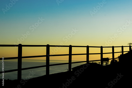 Silhouette of mountain road railing above sea at sunset, dramatic coastal travel landscape with vivid sky