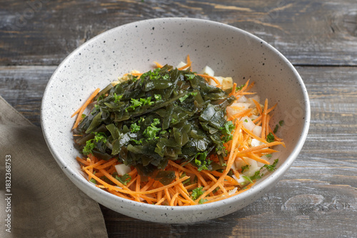 Seaweed salad ingredients with carrots, chopped eggs and diced onions in ceramic bowl on rustic wooden table