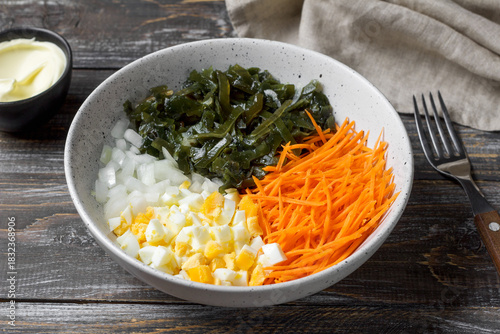 Fresh seaweed salad with shredded carrots, chopped eggs and onions in ceramic bowl on rustic wooden table