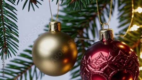 Close-up detail shot of shiny Christmas baubles hanging on a decorated tree, with soft warm lights creating festive bokeh in the background. Cozy holiday atmosphere
