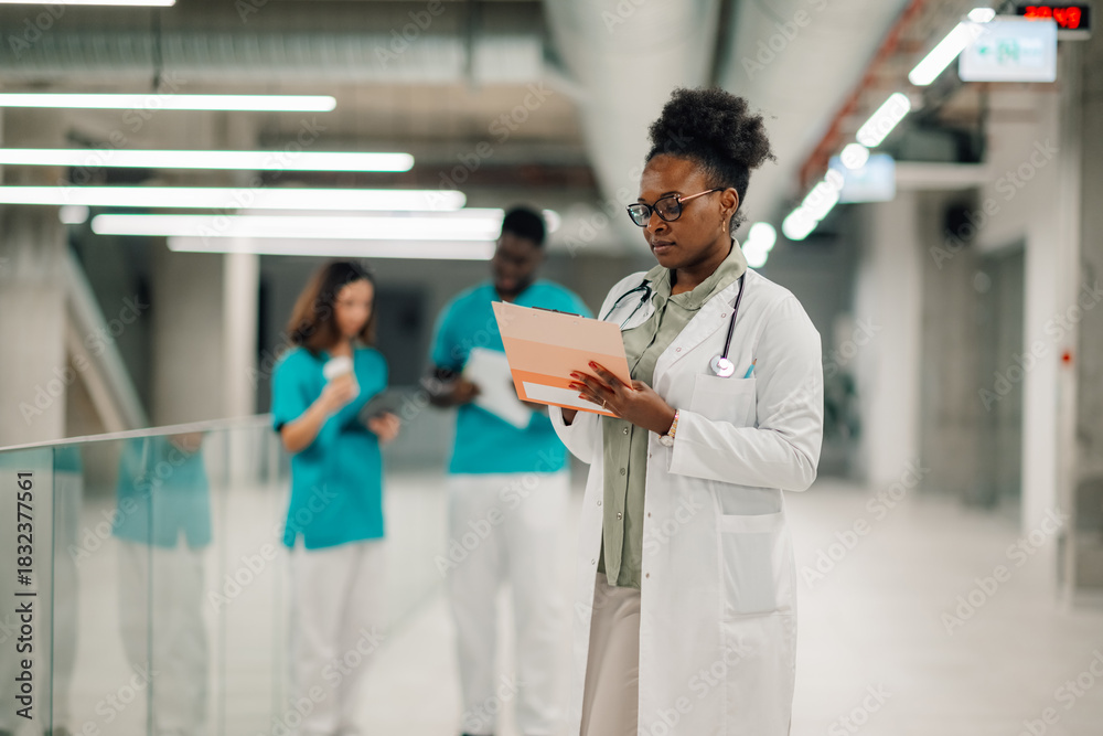 Fototapeta premium Female doctor reviewing medical records in hospital corridor