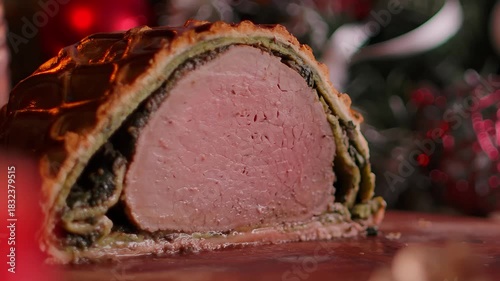 A spatula lifts a piece of Beef Wellington revealing juicy baked meat on a table with Christmas decorations and candles