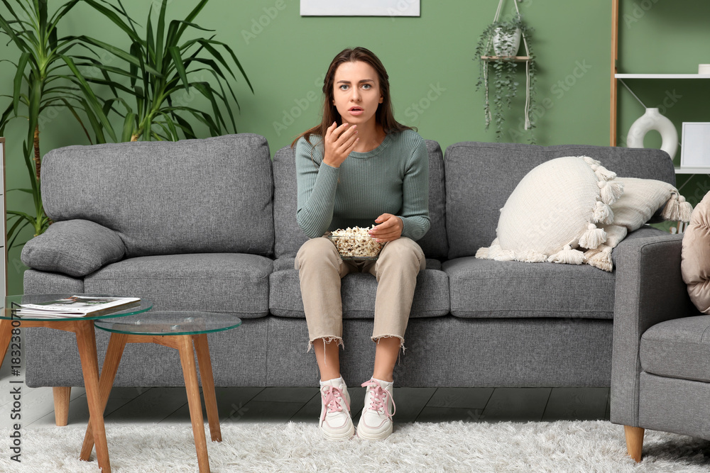 Obraz premium Upset young woman with popcorn watching movie on sofa at home