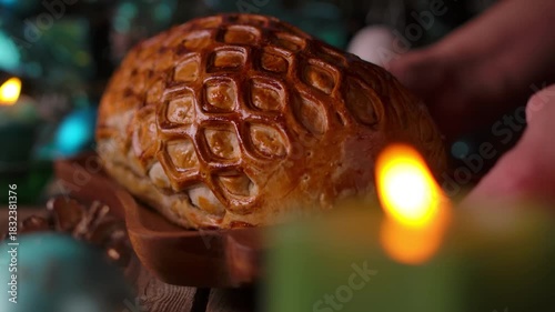A wooden plate with Beef Wellington is placed on a table with Christmas decorations, candles, spruce branches and a pine cone for a festive holiday dinner